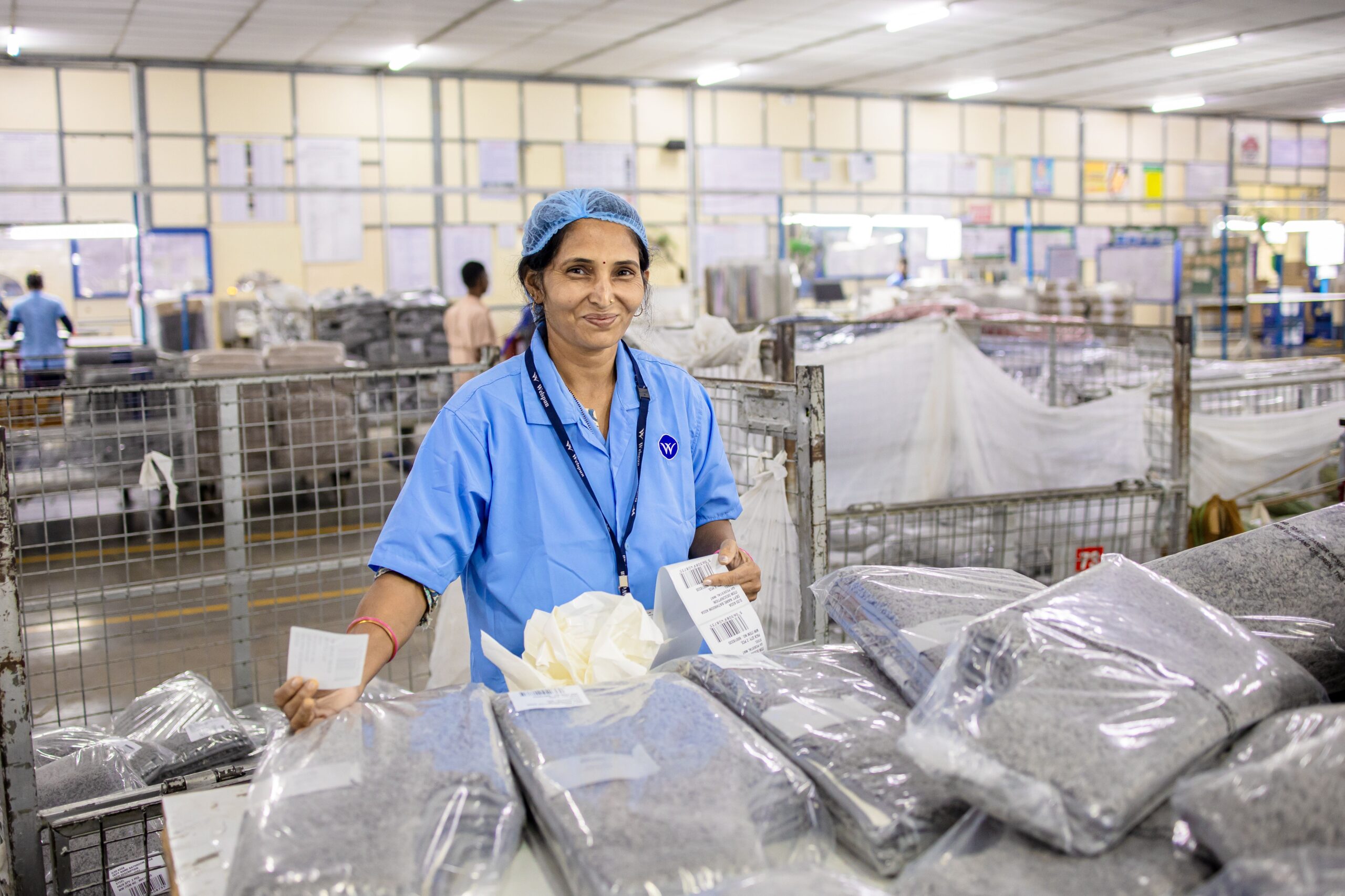 A female worker in blue uniform at a textile factory sorting packaged products.